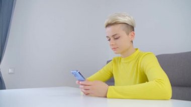 Cep telefonu uygulaması ile mesaj yazılıyor. Tom Boy saç stiline sahip genç beyaz kadın tecrit sırasında modern akıllı telefonu internet iletişimi için kullanıyor. Kısa saçlı güzel bir bayan cep telefonu kullanıyor.