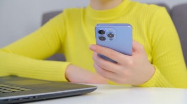 İnternette iletişim kurmak için modern cep telefonu kullanan genç bir kadın. Sosyal medya uygulamasındaki müşterilerle üçlü kameralı yeni akıllı telefondan iletişim kuran serbest çalışan kadın.