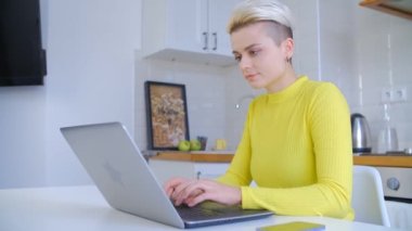 Kilit altında serbest çalışan beyaz bir kadın. Genç ve güzel bir kadın, kısa erkek gibi saç kesimi var. Uzak iş ve eğitim için modern dizüstü bilgisayarını kullanıyor. 4K stok videosunda.