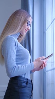 Sarışın kadının cep telefonu kullandığı dikey video. Modern akıllı telefon cihazına 4K stok görüntülerinde mesaj yazan güzel, genç bir kadın.