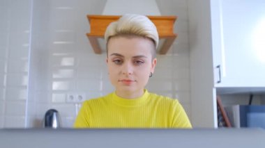 Kısa boyalı saçlı güzel erkek çocuk evde dizüstü bilgisayarla kilitli çalışıyor. Serbest çalışan kadın, 4K stok video ile mutfakta defter bilgisayarı üzerinde çalışıyor.