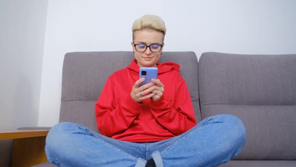 在智能手机社交媒体应用程序上输入评论的白人妇女 心情愉悦的汤姆男孩女孩 锁门时坐在沙发上 在现代手机上输入短发短信息 — 图库视频影像