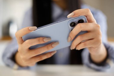 Akıllı telefondan oyun oynayan oyuncu kız. Evde video oyunu uygulaması oynamak için modern mavi cep telefonu kullanan genç bir kadın.. 