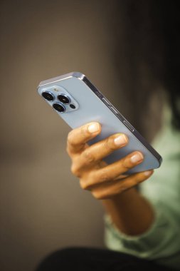 Üçlü kameralı cep telefonu kullanan siyah bir kadın. Genç Afrikalı kadın internet haberlerini modern mavi akıllı telefon cihazıyla tarıyor. Yeni cep telefonu aygıtıyla sosyal medya uygulamasına mesaj yazılıyor