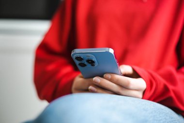 Üç kameralı cep telefonu kullanan genç bir kız. Beyaz kadın sosyal medya uygulamasında modern mavi akıllı telefon cihazına mesaj yazıyor. Kadın yeni cep telefonu aygıtıyla çevrimiçi iletişim kuruyor