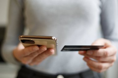 Kredi kartı ve cep telefonuyla ödeme yapan bir kadın. Modern akıllı telefonlu bir internet mağazasından müşteri satın alıyor. Kadın, cep telefonu uygulaması ve banka kartıyla para transferi yapıyor.