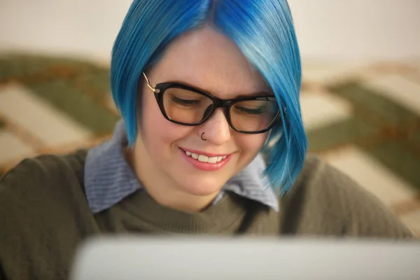 在笔记本电脑上工作的蓝头发的神经紧张的白人妇女 快乐的年轻人在家里的笔记本电脑上做自由职业工作 笑容满面的女性打字文字 — 图库照片