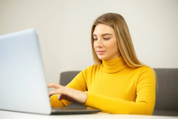 ロックダウン時に自宅でノートパソコンのキーボードを入力する美しいブロンドの女性 オンラインで遠くの仕事をしている陽気な起業家の人 若いです大人女性作業上の現代のノートPc上で笑顔 — ストック写真