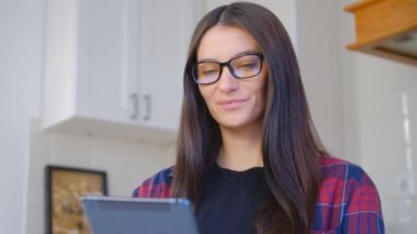 Tablet bilgisayarından 5G internete bağlanan gözlüklü güzel inek kadın. Beyaz esmer kişinin portresi cep telefonuyla haberlere bakıyor. Evden internet üzerinden iletişim kuran çekici bir kadın.