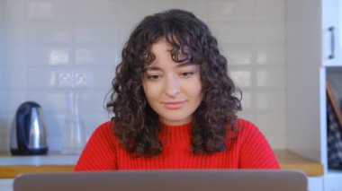 Laptopta çalışan güzel esmer kadın. Not defterine yazı yazan kıvırcık siyah saçlı güzel beyaz bir kadın. Tecrit sırasında internetten çalışan genç bir serbest çalışanın 4k videosu