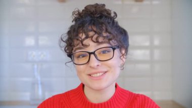 Gözlüklü mutlu beyaz esmer web kamerasından konuşuyor. Neşeli ve duygusal bir kadın, kıvırcık saçlı, video konuşmasında konuşuyor. Bukleli güzel bir kadının portresi duygusal konuşma yapıyor.