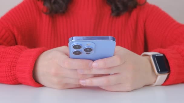 女の子は携帯電話にメッセージを入力します 現代的な青のスマートフォンを使用して 赤いセーターの若い白人女性がオンラインで通信します 4Kストックビデオの女性の書き込みコメント上のソーシャルメディアアプリ — ストック動画