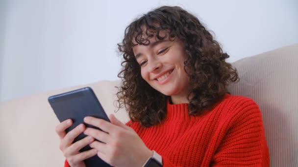 おもちゃの笑顔でタブレットPcを使用して幸せな白い女性 現代のポータブルデバイス上で高速5Gのインターネットを閲覧巻き毛を持つ陽気な若い女性 かわいい白人ブルネットは良いニュースをオンラインで読む — ストック動画