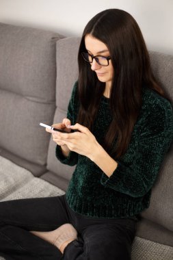 Beyaz kadın cep telefonundan mesaj yazıyor. Uzun boylu esmer kadın tecrit sırasında iletişim kurmak için modern akıllı telefonu kullanıyor. Sosyal medya uygulaması üzerinden iletişim kuran güzel bir yetişkin modeli.