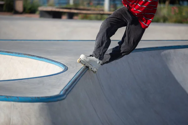 Inline skater doing trick in outdoor skatepark. In-line roller blader performing top acid grind on rail in concrete mini ramp