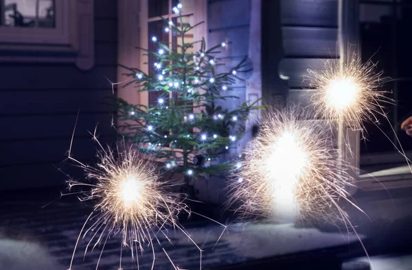 Sparklers on the background of a Christmas tree on the terrace of a wooden house on a winter evening, toned in the color of the year 2022 — Stock Photo, Image