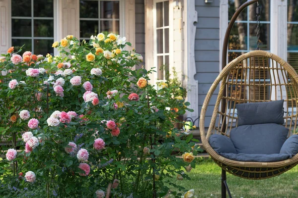 Romantische Sitzecke im Rosengarten, runder Holztisch und Stühle neben den großen blühenden Rosensträuchern — Stockfoto