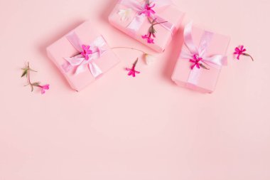 Şenlikli pembe arka plan. Saten fiyonklu bir hediye ve açık pembe pastel arka planda pembe küçük çiçekler..