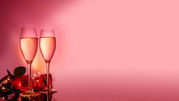 Ποτήρια σαμπάνιας, κόκκινα τριαντάφυλλα μπροστά σε ροζ μπεζ φόντο. Ημέρα του Αγίου Βαλεντίνου σύνθεση διακοπών. Γενέθλια, Γυναικεία, γαμήλια ημέρα έννοια. — Φωτογραφία Αρχείου