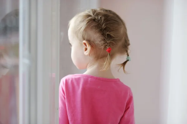 Schattig klein meisje door het venster — Stockfoto