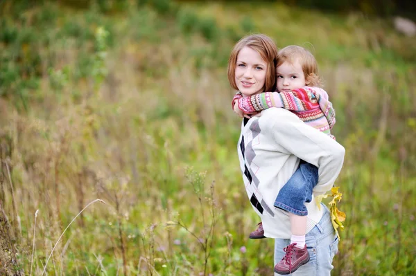 Ein Mädchen mit einer Huckepackfahrt auf ihrer Mutter — Stockfoto