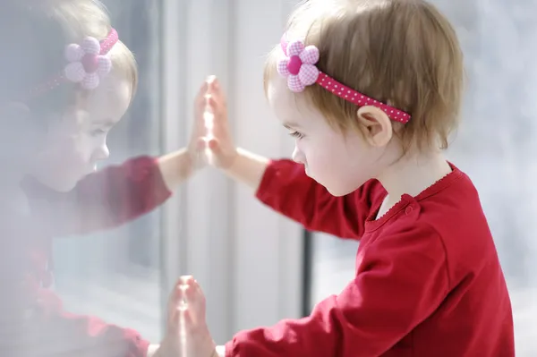 Little toddler girl looking through a window — Stock Photo, Image