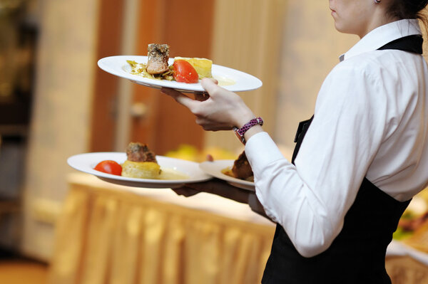 Waitress carrying three plates with meat dish
