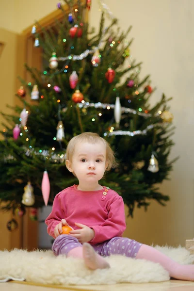 幼児の女の子がクリスマス ツリーの下に座っています。 — ストック写真