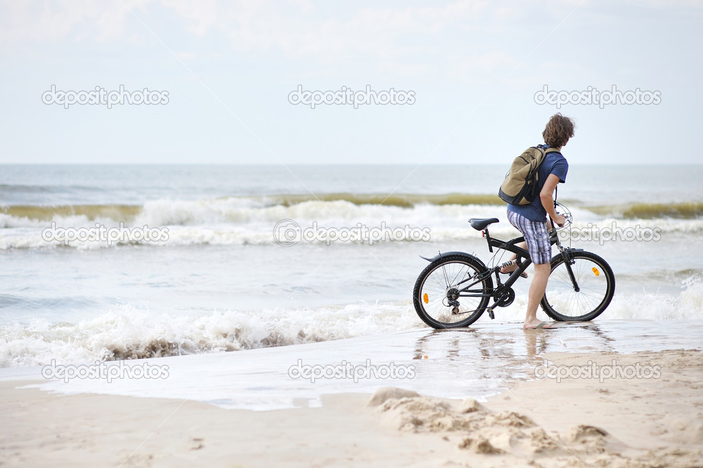Young man bicycling along al beach