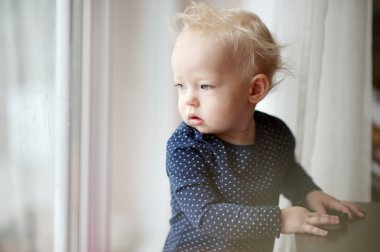 Adorable toddler girl looking through the window clipart