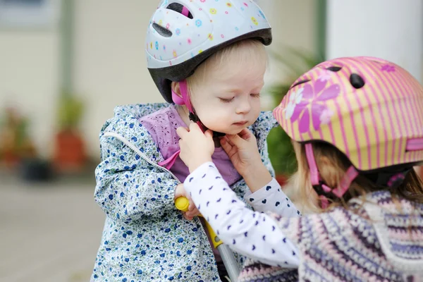 Kleines Mädchen hepst ihre Schwester, damit sie einen Helm aufsetzt — Stockfoto