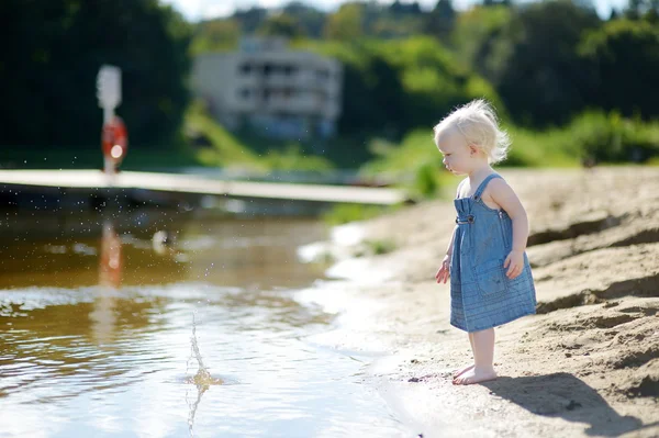 Adorable girl throwing stones into river — Stock Photo, Image