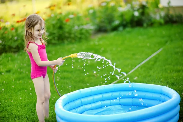 Klein meisje gieten van water in een pool — Stockfoto