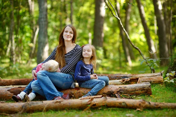 Two sisters and their mother sitting on a big log — Stock Photo, Image