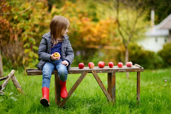 Kleines Mädchen sitzt im Herbst auf einer Holzbank — Stockfoto