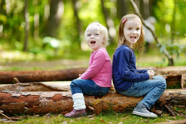 Zwei kleine Schwestern sitzen auf einem großen Baumstamm — Stockfoto