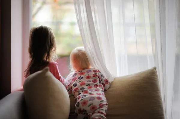 Twee kleine meisjes kijken uit het raam — Stockfoto