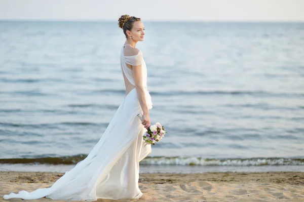 Bride walking along sea coast on sunset — Stock Photo, Image