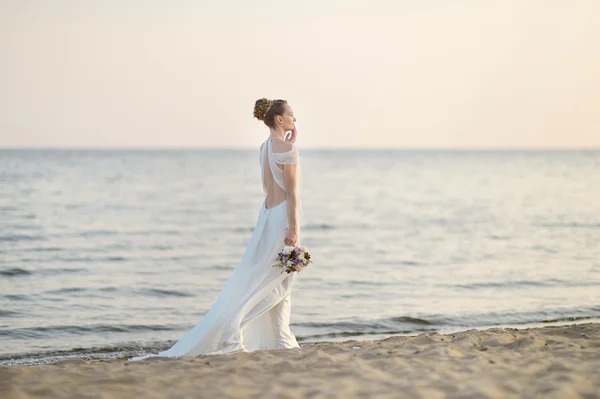 Bride walking along sea coast on sunset — Stock Photo, Image