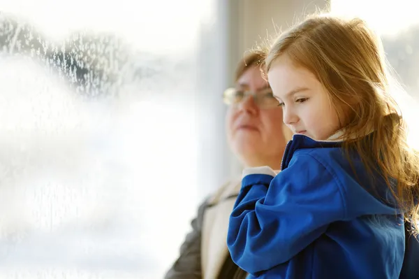 Klein meisje en oma staren door een raam — Stockfoto