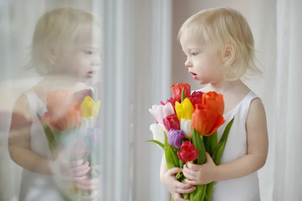 Adorable niña con tulipanes junto a la ventana — Foto de Stock