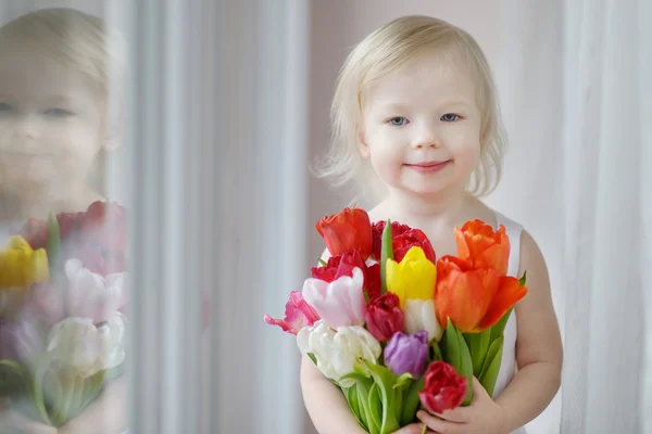 Schattig peuter meisje met tulpen door het venster — Stockfoto