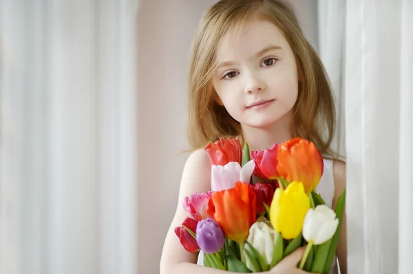 Schattig meisje met tulpen door het venster — Stockfoto