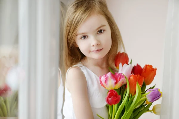 Entzückendes kleines Mädchen mit Tulpen am Fenster — Stockfoto