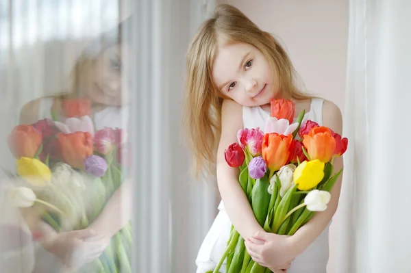 Schattig meisje met tulpen door het venster — Stockfoto