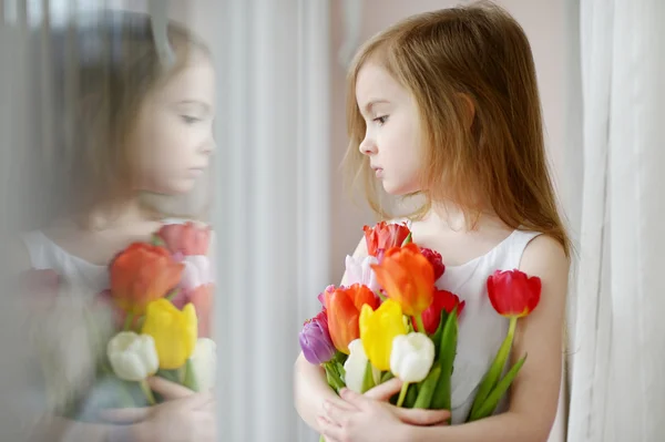 Entzückendes kleines Mädchen mit Tulpen am Fenster — Stockfoto