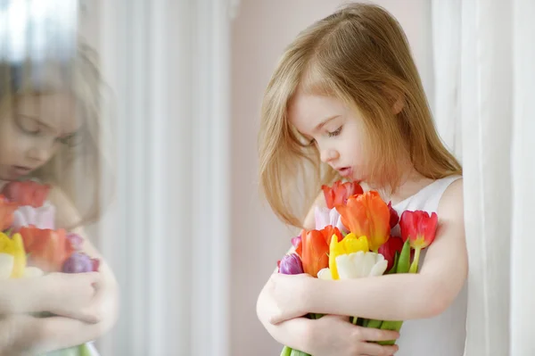 Entzückendes kleines Mädchen mit Tulpen am Fenster — Stockfoto