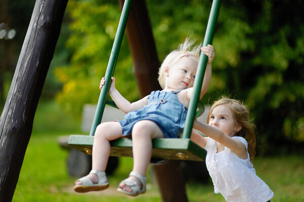 Two little sisters having fun on a swing