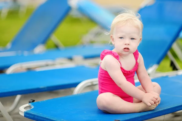 Niña sentada en una tumbona junto a una piscina — Foto de Stock