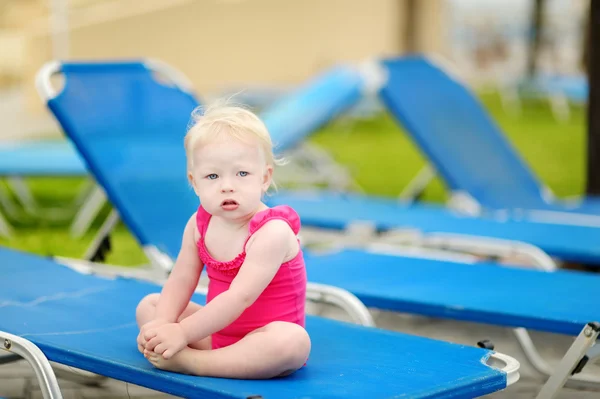 Niña sentada en una tumbona junto a una piscina — Foto de Stock